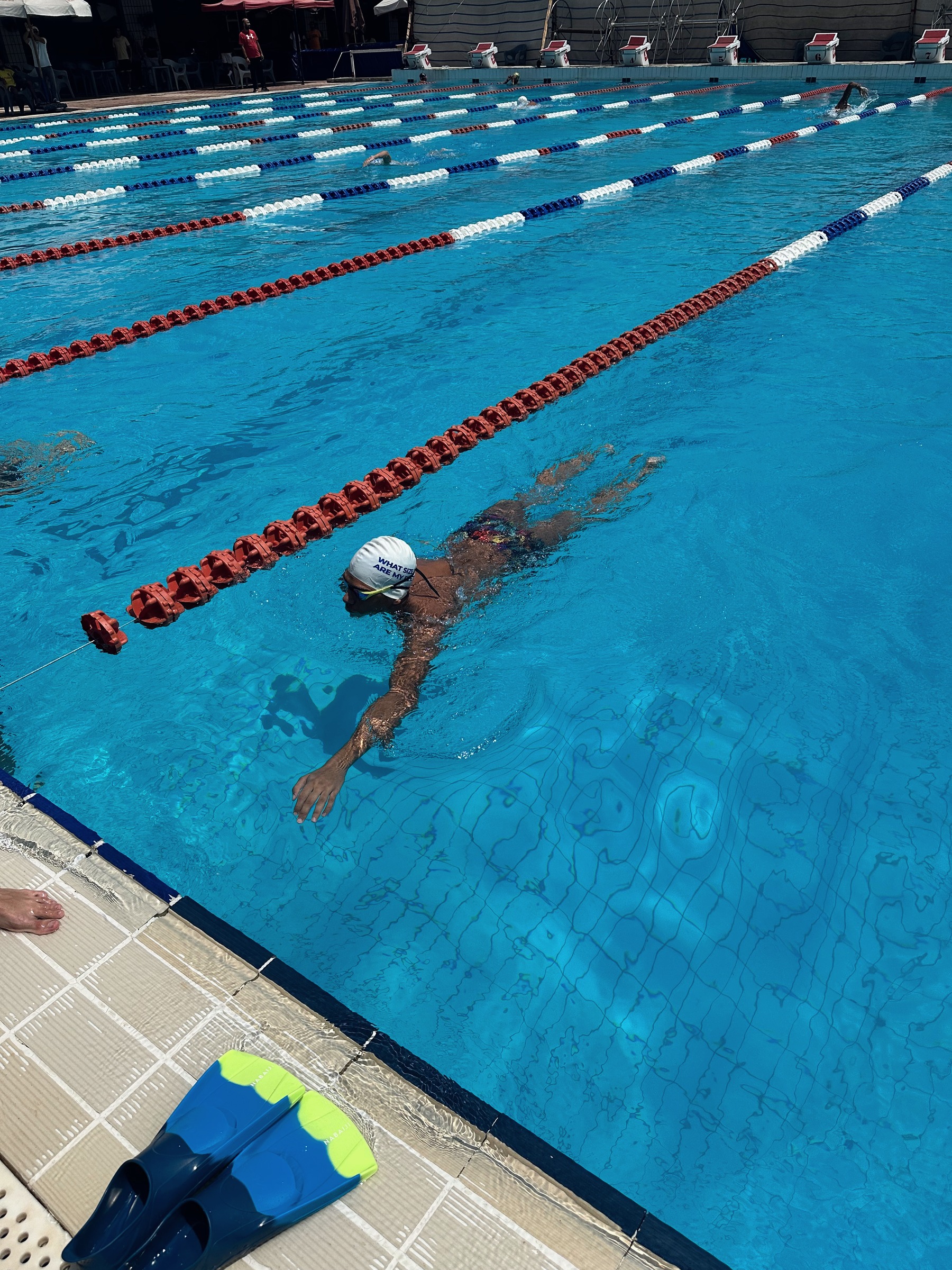 A swimmer training in a lane, a pair of fins waiting on the deck