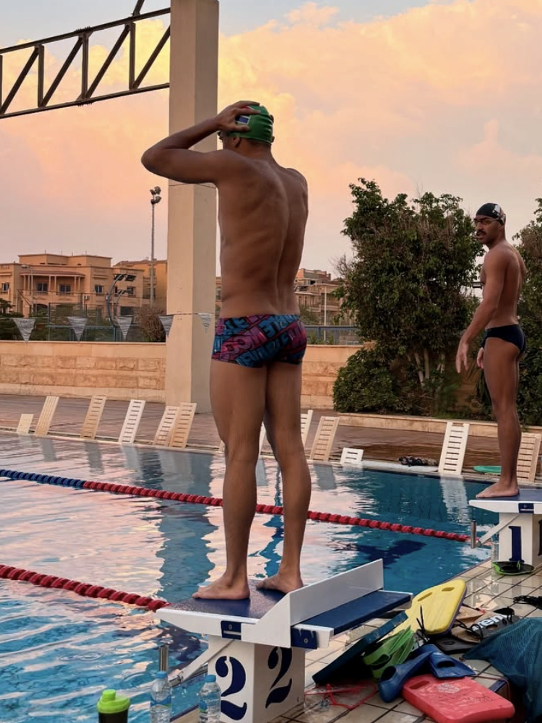A swimmer on the block at sunset, fins and kickboards on the deck at his feet