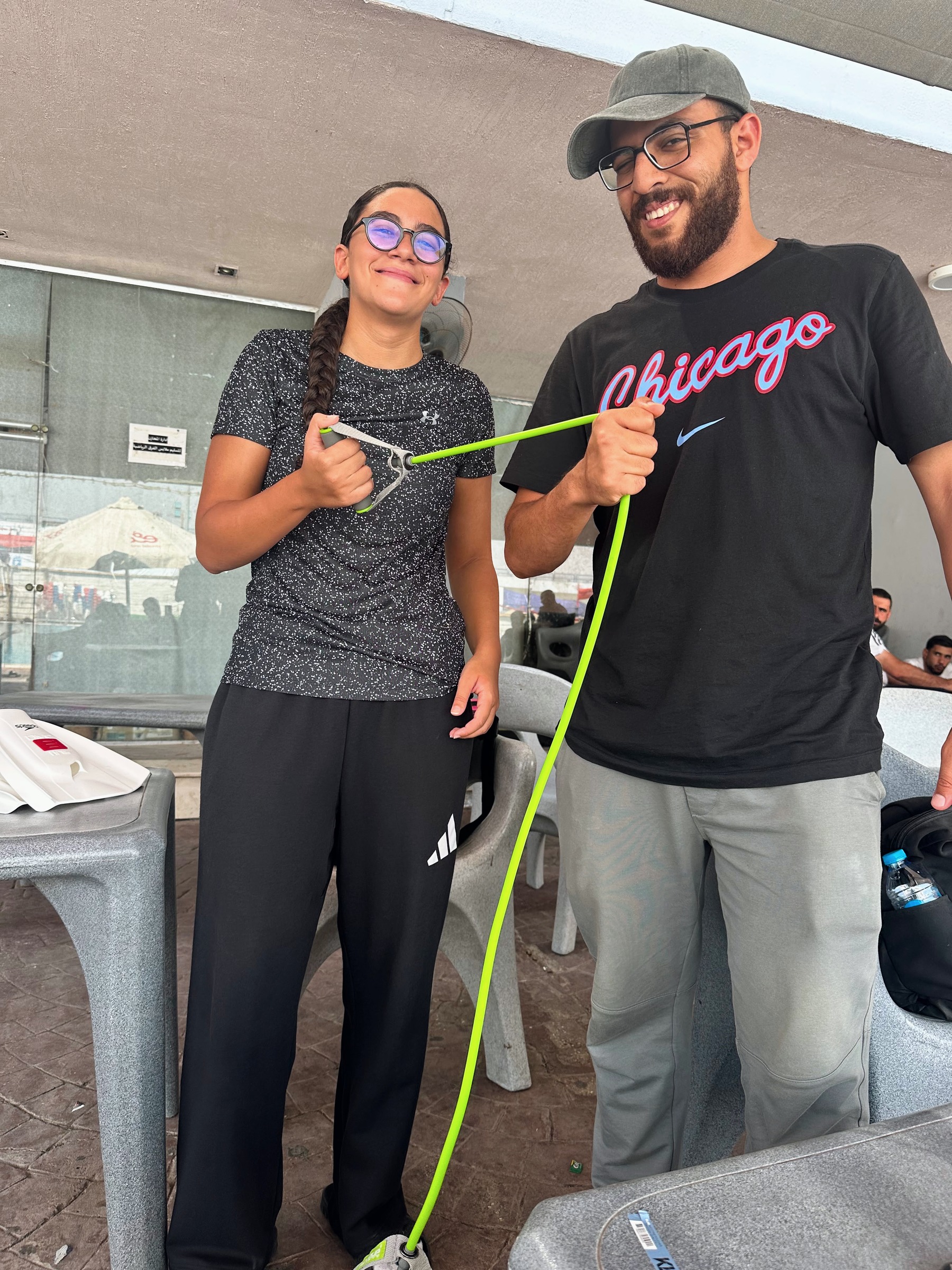 Coach Ali Hany holding a resistance band for a swimmer's warm-up on the pool deck